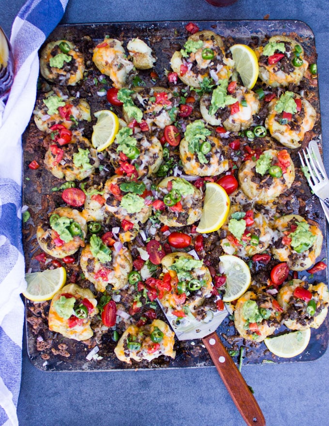 A baking sheet out of the oven with all the smashed potatoes and topping ready