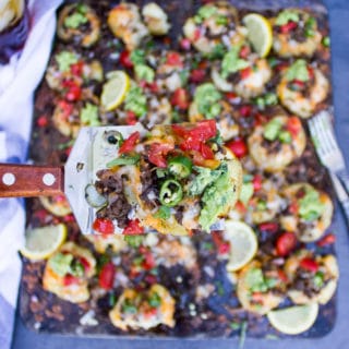 A spatula holding one smashed potato loaded with toppings and highlighting it