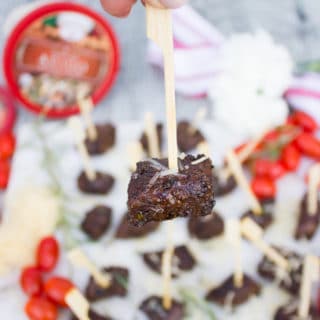 A hand holding a steak bite on a stick showing the cheese sprinkle