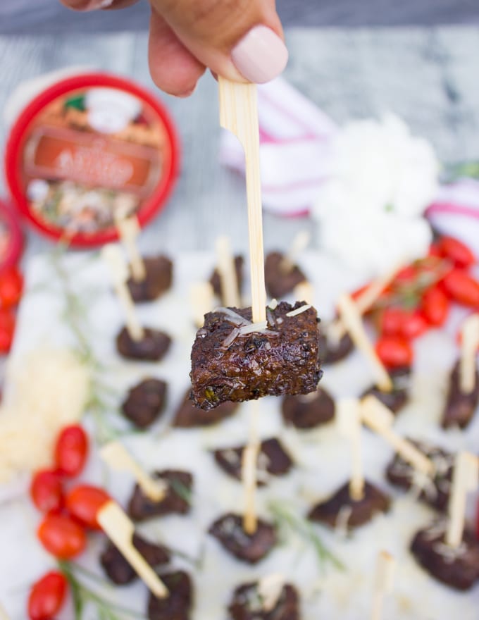 A hand holding a steak bite on a stick showing the cheese sprinkle