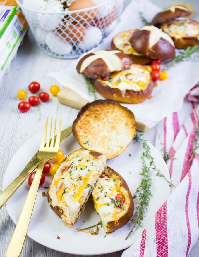 Baked eggs in bread bowl on a white marble, a tea towel and a fork and spoon cutting the bread