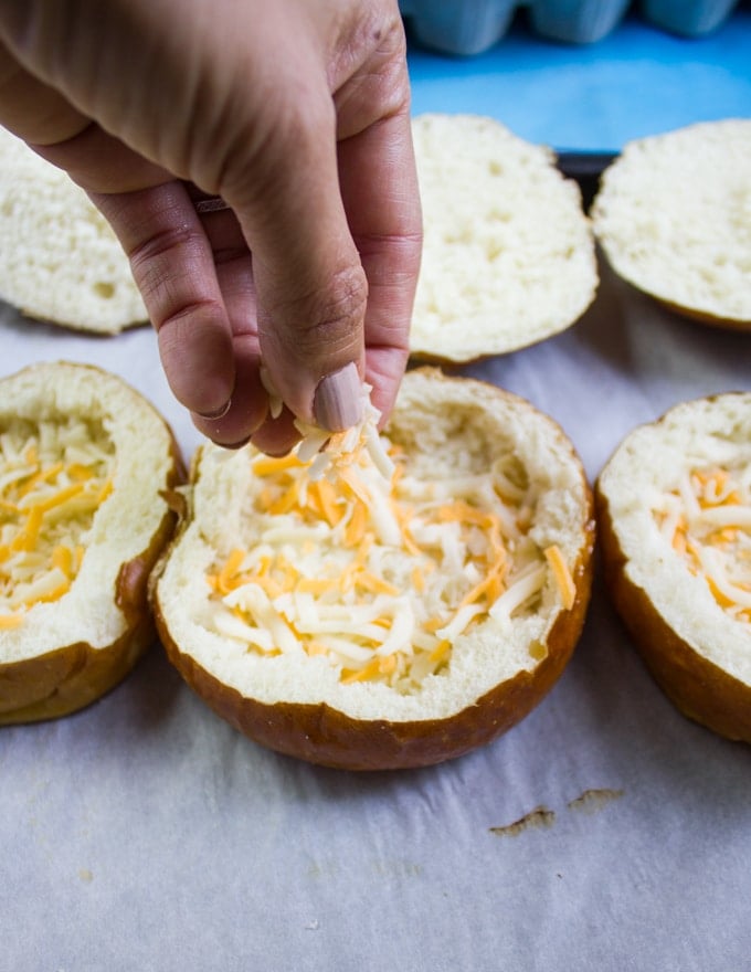 A hand sprinkling cheese at the bottom of the bread bowls
