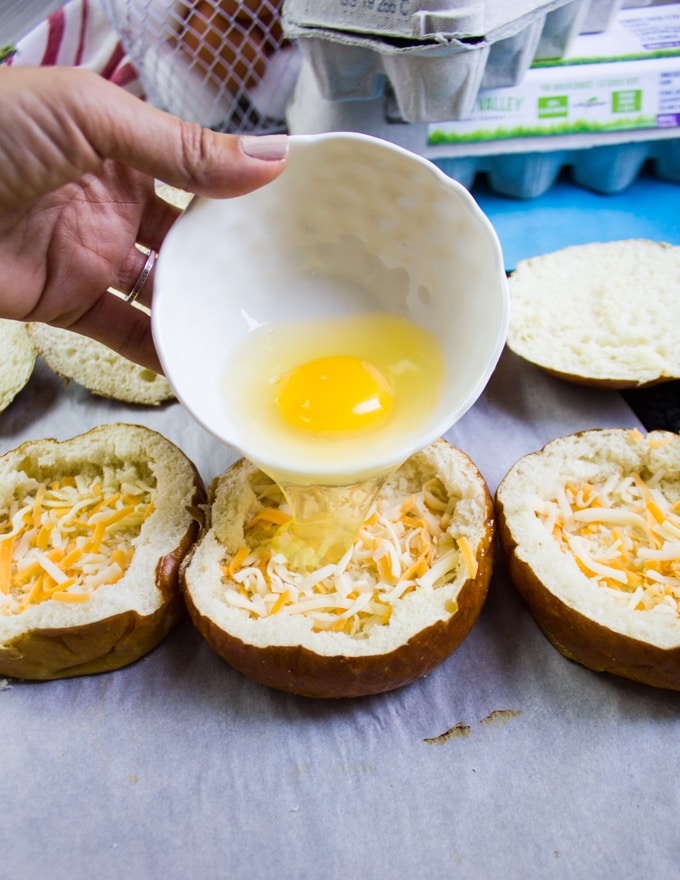 A hand pouring an egg in each bread bowl