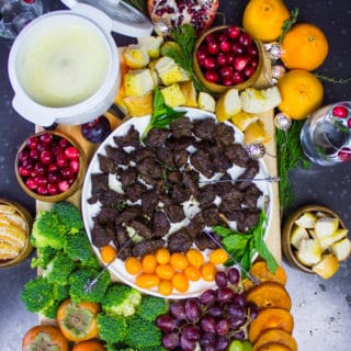 board of cheese fondue with cheese fondue dippers incuding lamb chunks, fruits and veggies and croutons.