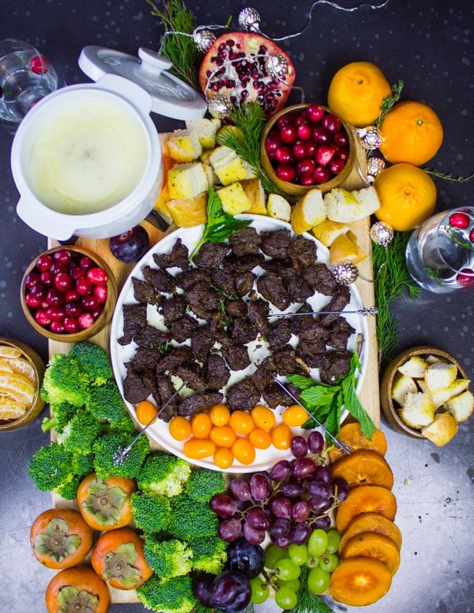 board of cheese fondue with cheese fondue dippers incuding lamb chunks, fruits and veggies and croutons.