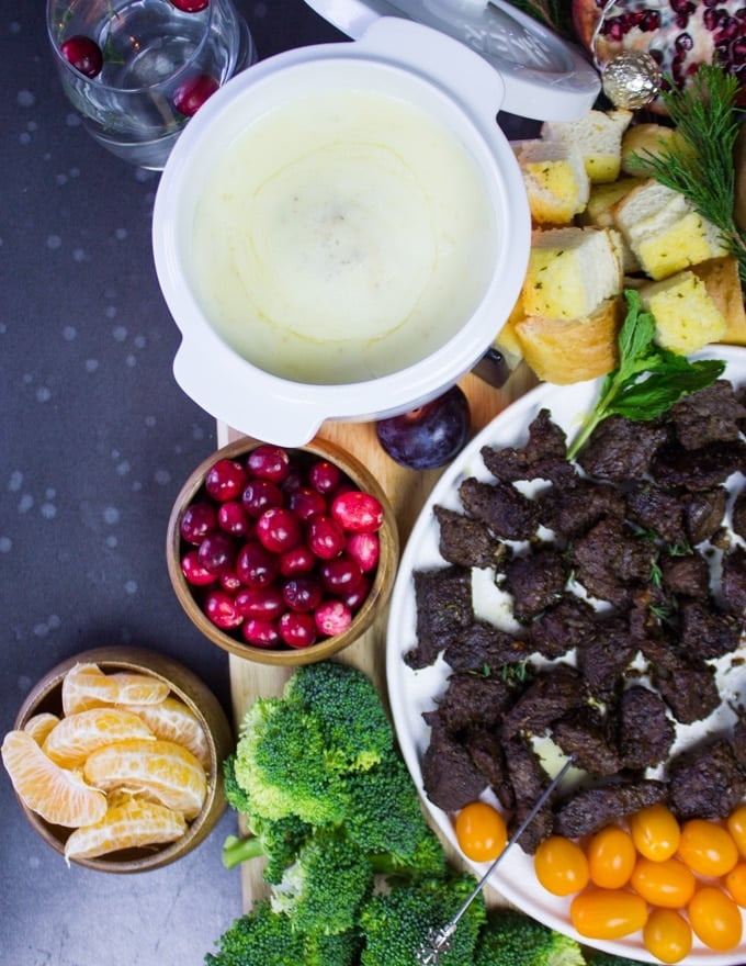 A white pot of cheese fondue next to cranberries and fruits dippers