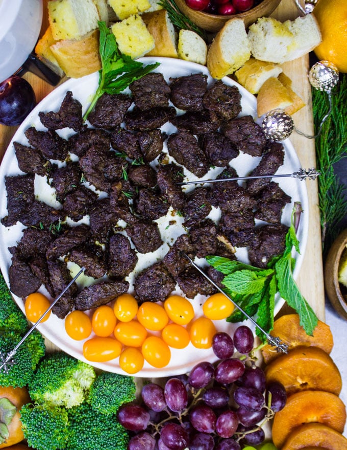 Plate of lamb dippers surrounded by fondue forks, broccoli and yellow tomatoes