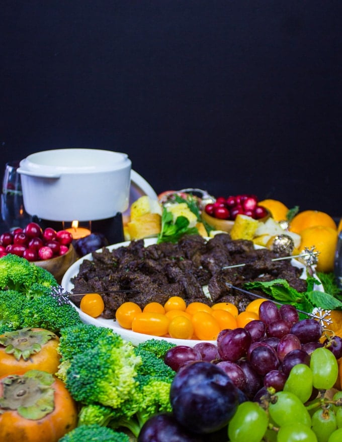 A side view of the cheese fondue platter with the pot of cheese fondue and all the veggies and fruits around it.