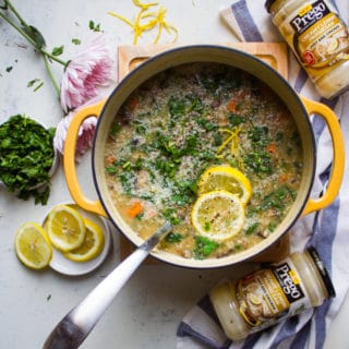 A large pot of soup with a ladle in the middle. Lemon slices are topped on the minestrone soup and surrounded by parsley and more lemons
