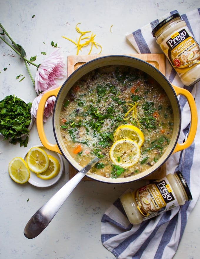 A large pot of soup with a ladle in the middle. Lemon slices are topped on the minestrone soup and surrounded by parsley and more lemons