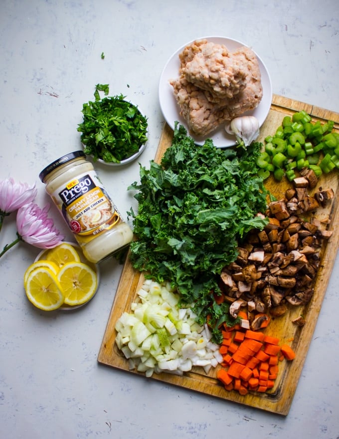 Ingredients for the soup chopped on a cutting board, such as chopped kale, mushrooms, carrots, onions, herbs 