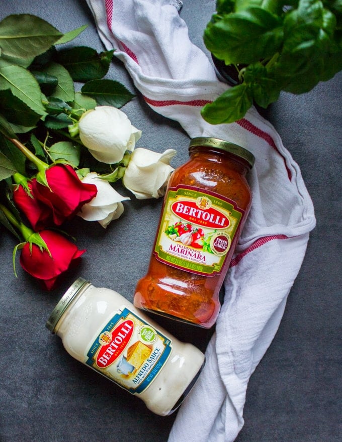 two jars of bertolli sauces next to a bunch of roses