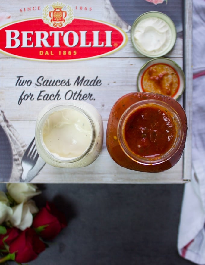 two jars of Bertolli sauces, one marinara sauce and one alfredo sauce opened up to show the inside