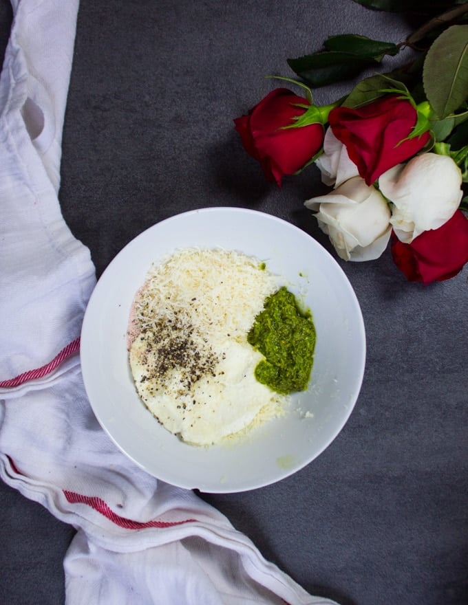 a bowl with the filling ingredients: ricotta, basil pesto, parmesan cheese. surrounded by a bunch of roses