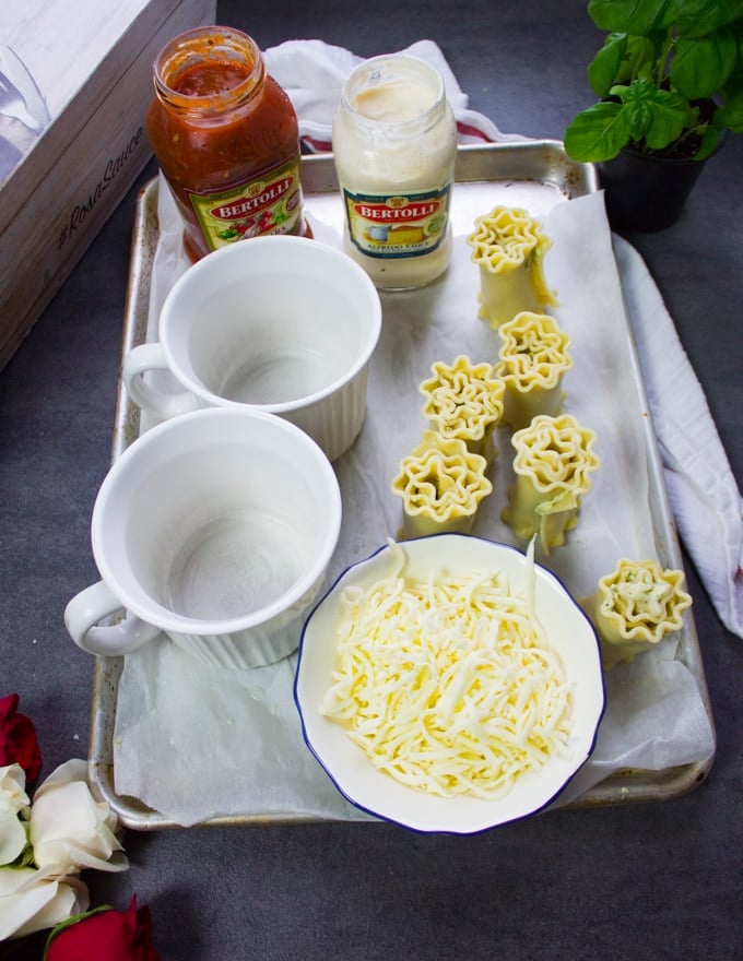 A tray with two mugs, a bowl of cheese, the ready lasagna roll ups and the sauces