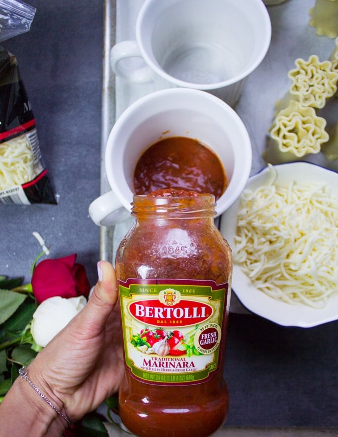 A hand Pouring in the marinara sauce at the bottom of the mug