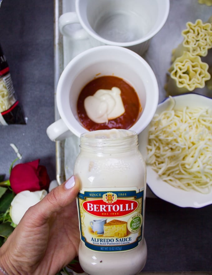 A hand pouring the alfredo sauces over the marinara sauce in the mug