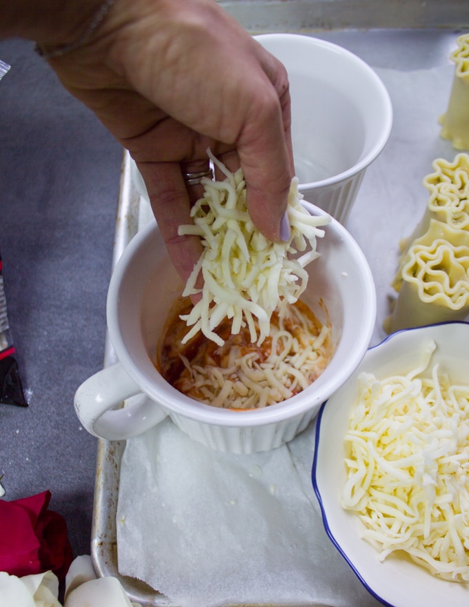 A hand sprinkling cheese at the bottom of the mug over the rosa sauce