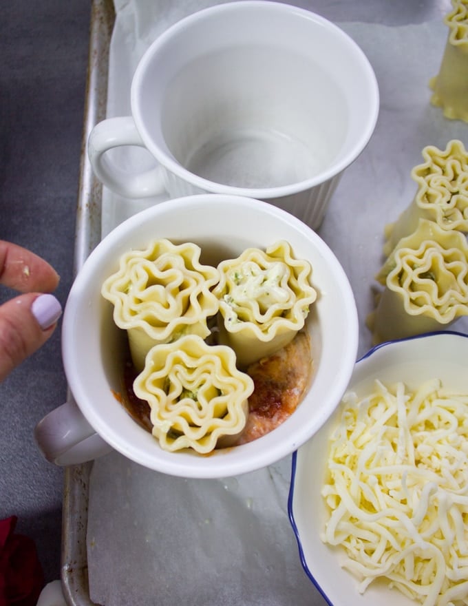 Lasagna rolls ups being stacked in the mug over the rosa sauce and cheese