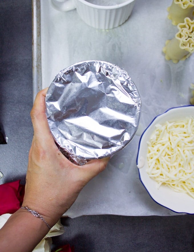 A hand covering the mugs with foil before baking