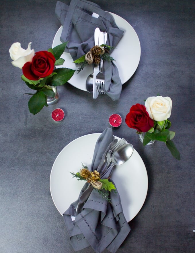 A table set up for two for valentine's day at home with plates, napkins or roses