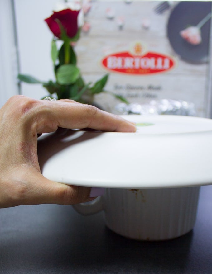 A hand holding a plate over the mug ready to flip