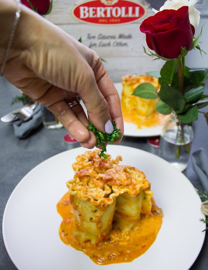 A hand sprinkling fresh basil over the lasagna for garnish