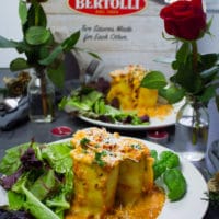 A plate with lasagna rolls ups, a salad and a vase of roses