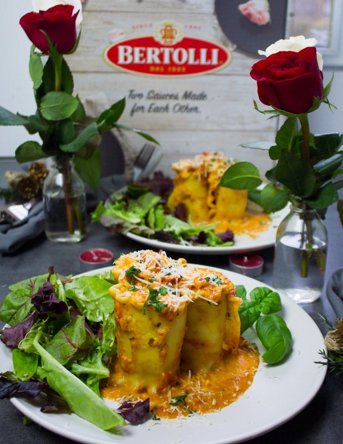 A plate with lasagna rolls ups, a salad and a vase of roses