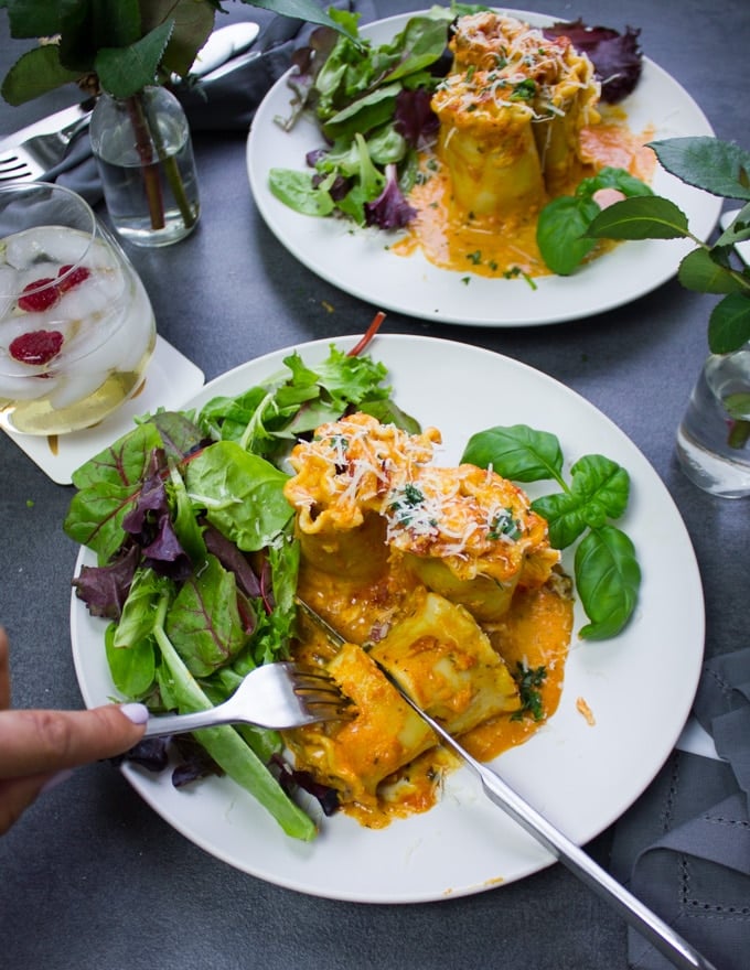 A hand using fork and knife to cut the lasagna roll ups