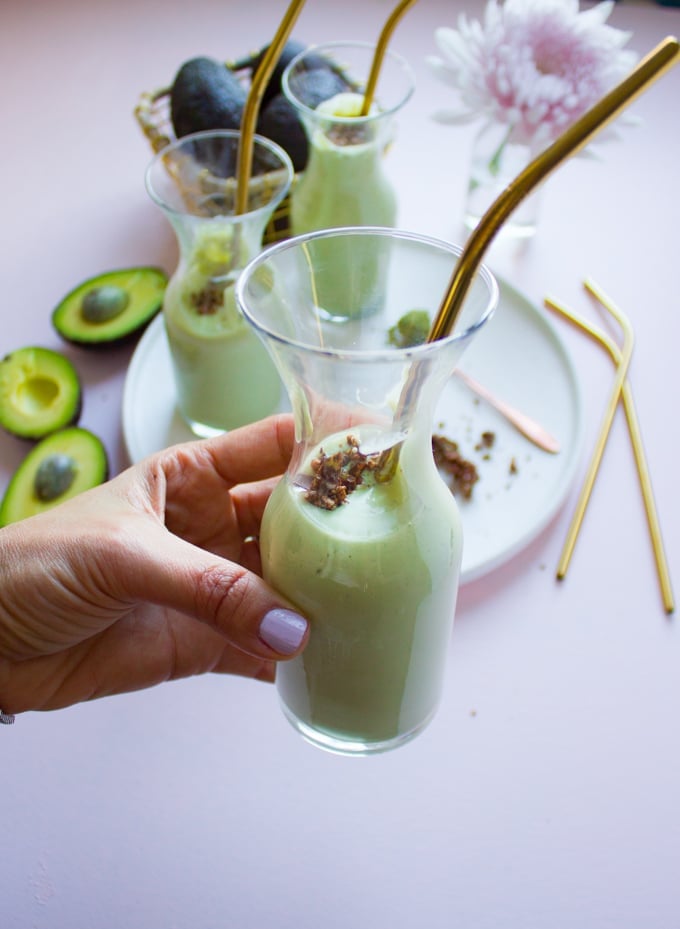 A hand holding an avocado smoothie cup with a straw