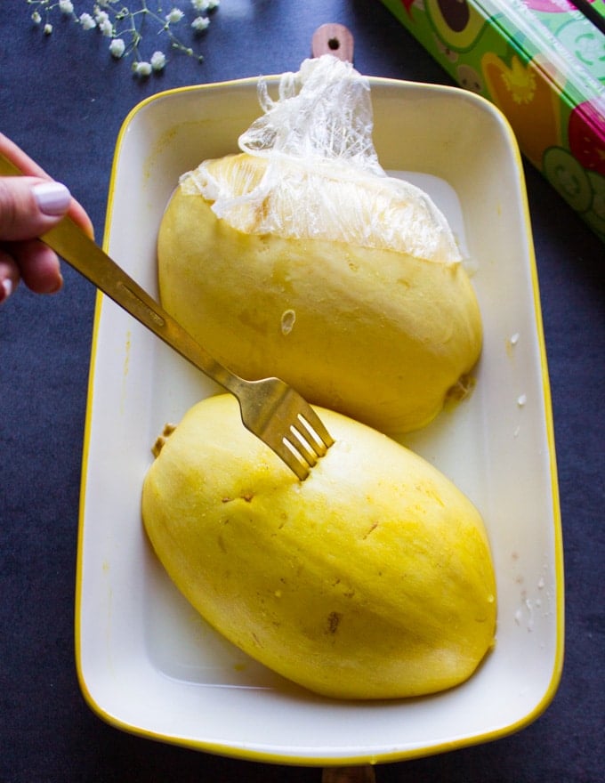 A fork piercing in a spaghetti squash half to make sure it's cooked through