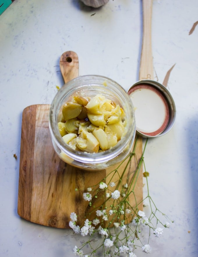 Roasted garlic in a mason jar ready for the olive oil on a cutting board
