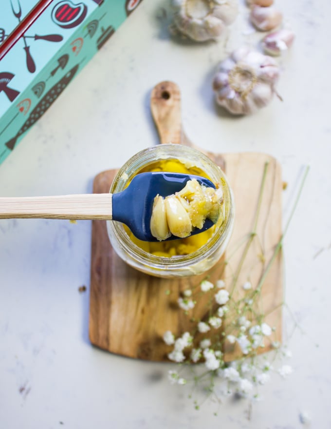 A spatula scoping some roasted garlic form the jar 