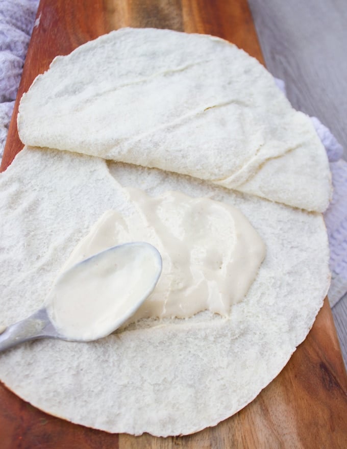 A spoon spreading tahini sauce over pita bread