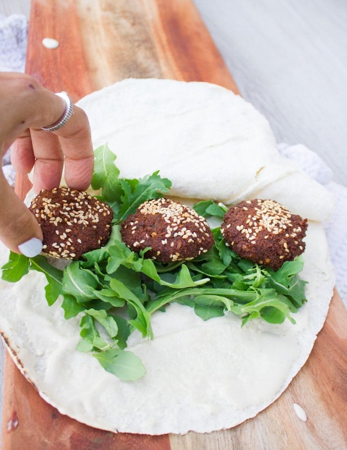 A hand putting falafel and arugula over the sandwich