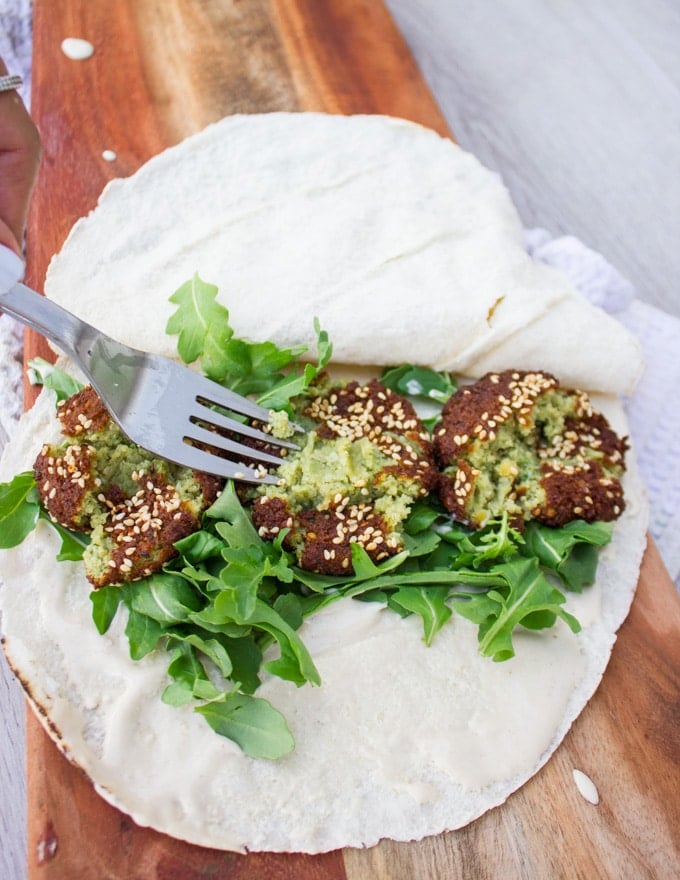 A fork mashing the falafel inside the sandwich before piling the topping