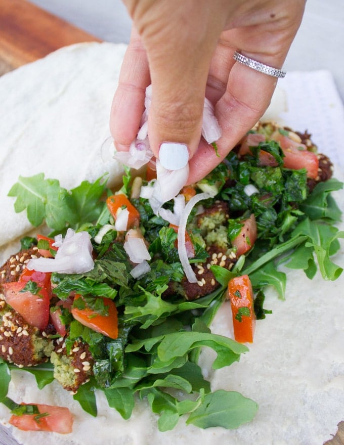 A hand piling on red onions and tabouleh salad over the falafel