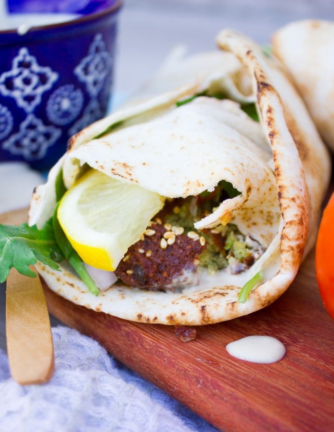 A close up of a falafel sandwich showing the tahini sauce on the snadwich and dripping on a cutting board next to the sandwich