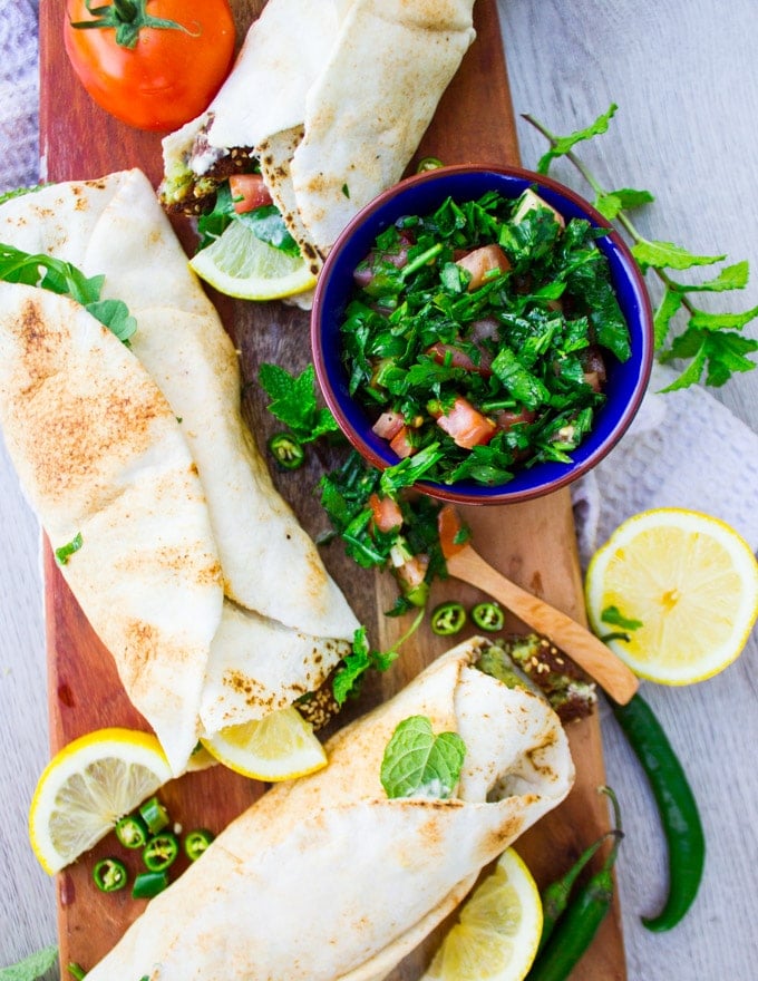 A close up of falafel sandwich next to a bowl of tabouleh salad