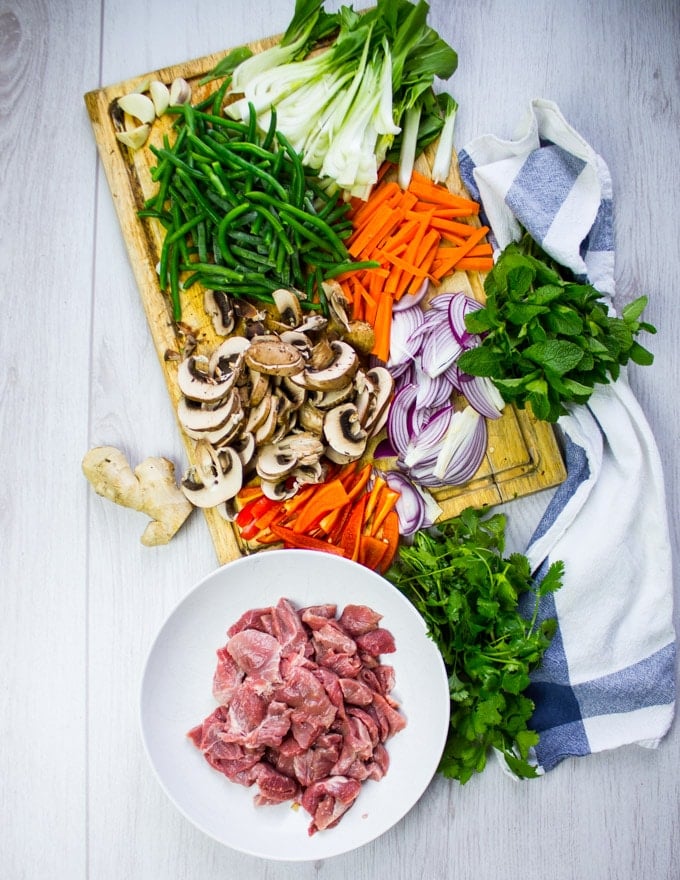 A bowl of thinly sliced lamb and a board with all the veggies ready to be used for the stir fry