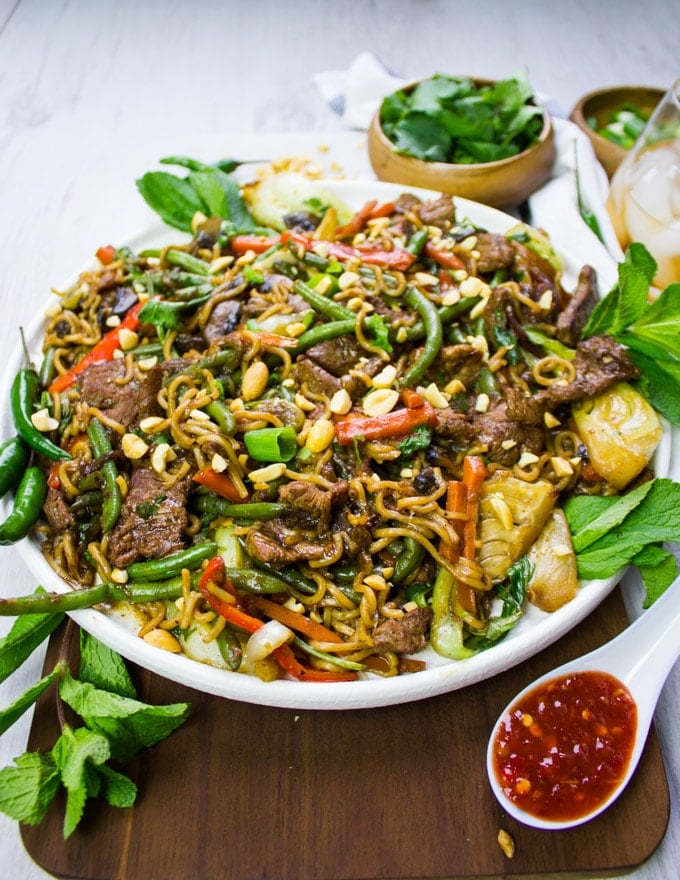 A plate of stir fry ready with cilli sauce and fully garnished with cilantro, mint and peanuts