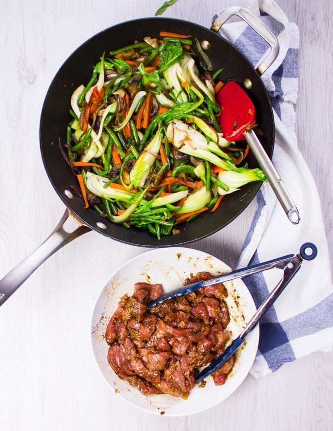 The stir fry veggies are cooked in a wok, and thelamb is marinating and ready to cook