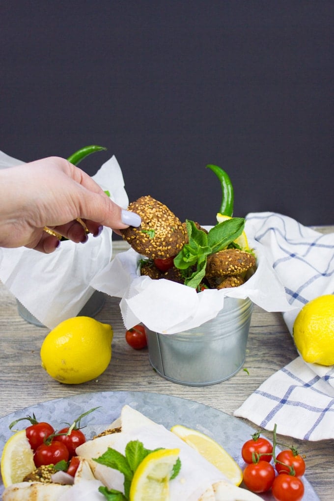 A bucket of falafel surrounded by a lemon and sprigs of mint