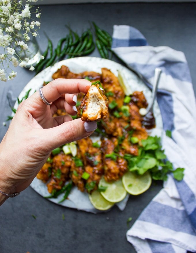 A hand holding a piece of fried Korean Chicken bitten to show the inside
