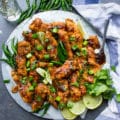 A plate of Korean Fried Chicken strips topped with cilantro and spread with lemon slices, green chillies and a kitchen towel.