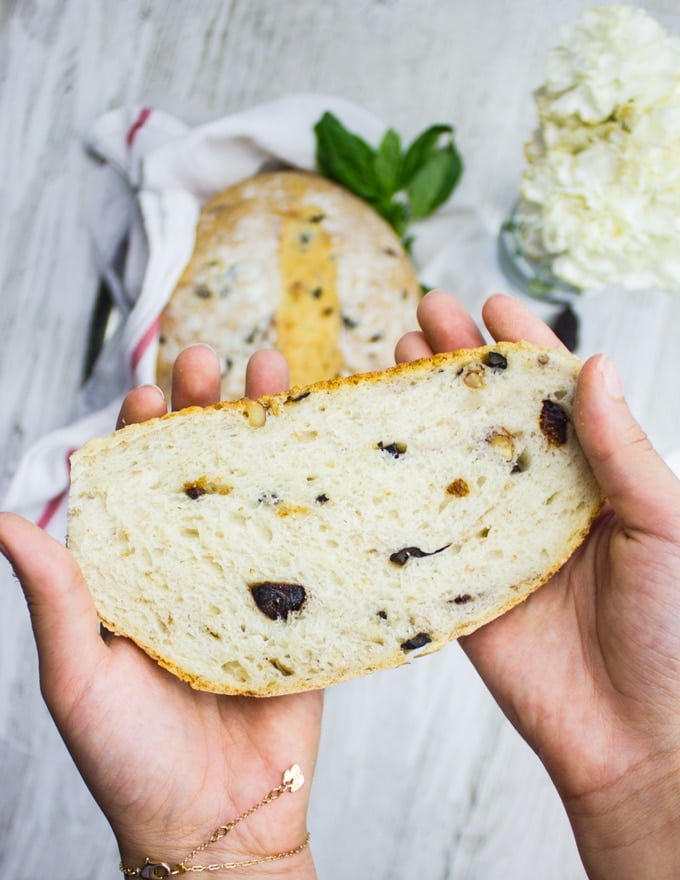 Two hands holding a loaf of bread up close showing the texture and additions of the bread