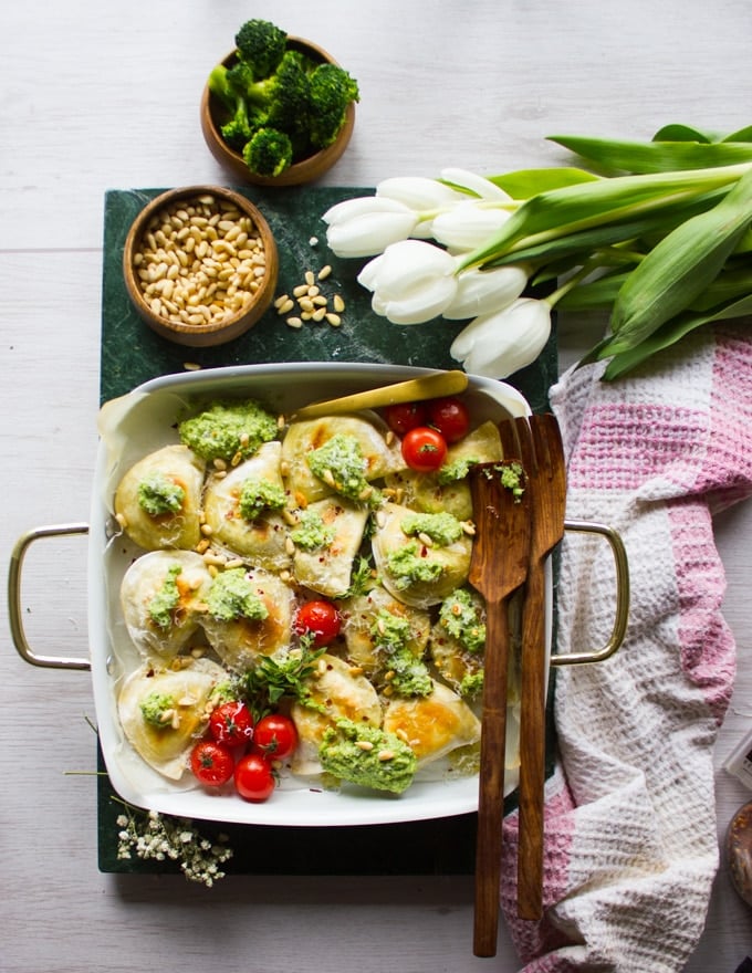 One pan baked pierogies with the broccoli pesto and pine nuts, surrounded by white tulips and a kitchen towel 