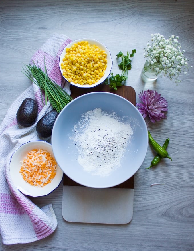 Ingredients for the corn fritters : a bowl with flour baking powder, corn in a bowl and shredded cheese