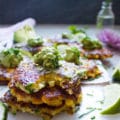 a stack of corn fritters with the last one bitten up to show the texture and a dollop of guacamole
